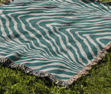 Zoe Animal Print Cotton Blend Blanket Throw in Teal, draped over a chair
