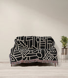 Diof Abstract Print Cotton Throw Blanket in Black and Beige, draped over a sofa