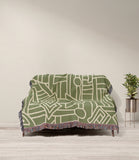 Diof Abstract Print Cotton Throw Blanket in Olive Green and Beige, draped over a sofa