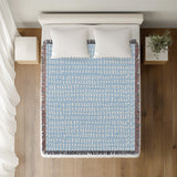 Kola Abstract Print Cotton Throw Blanket in Sky, on a bed