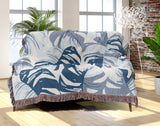 Monstera Leaf Cotton Throw Blanket in Blue, draped over a sofa