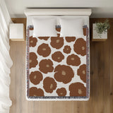 Poppi Floral Cotton Throw Blanket in Rust Brown, on a bed