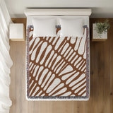 Pyro Abstract Print Cotton Throw Blanket in Rust Brown, on a bed