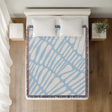 Pyro Abstract Print Cotton Throw Blanket in Sky, on a bed