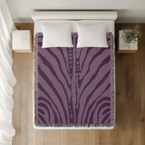 Sasha Zebra Print Cotton Throw Blanket in Purple, on a bed