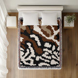 Sassi Animal Print Cotton Throw Blanket in Black, Rust Brown and Beige, on a bed