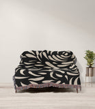 Nami Abstract Floral Blanket Throw in Black and Beige, draped over a sofa
